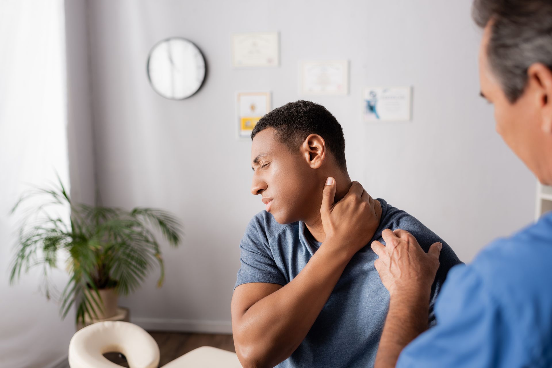 An injured man is touching his neck near a doctor, who's going to provide neck pain treatment.
